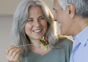older couple smiling at each other with woman feeding man some salad