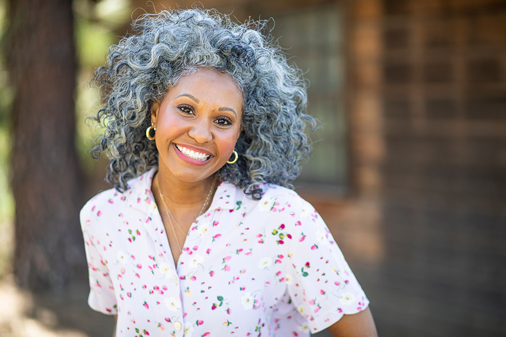 mature smiling black woman in a white shirt and grey curly hair